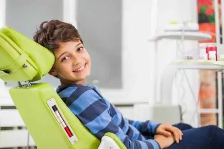 criança sorrindo e sentada na cadeira do dentista